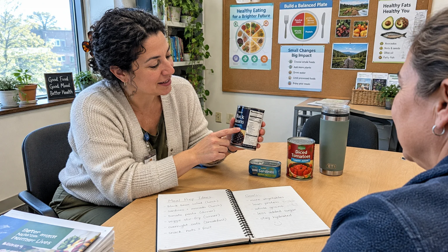 A nutritionist points to a can of black beans while counseling a patient seated across a table with meal planning notes.